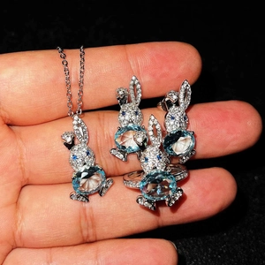 Sparkling rabbit jewelry set with blue topaz stones held in hand against black background