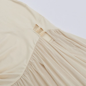 Detail of light beige dress featuring delicate pleats, mesh cutouts, and bead decorations
