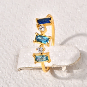 Macro d'une bague dorée avec pierres bleues taille émeraude et zircons blancs sur support