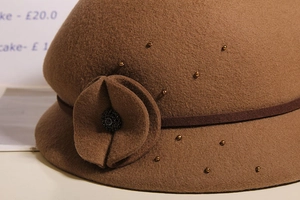Dettaglio ravvicinato di un cappello in feltro marrone caffè con perline e bottone floreale