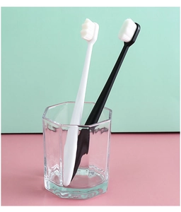 Close-up of black and white nano toothbrushes with dense soft bristles in a glass cup