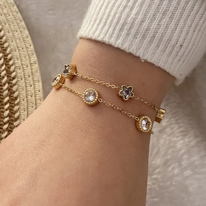 Détail d'un bracelet double chaîne dorée avec des breloques étoile et zircon rond