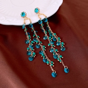Detailed view of peacock blue crystal tassel earrings on elegant brown satin silk