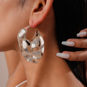 Gros plan de grandes boucles d'oreilles argentées irrégulières avec texture martelée