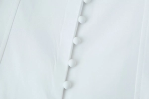 Close-up of elegant fabric-covered buttons and woven texture on white V-neck jacket