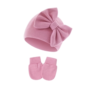Close-up of pink baby knitted hat with big bow and matching anti-scratch mittens