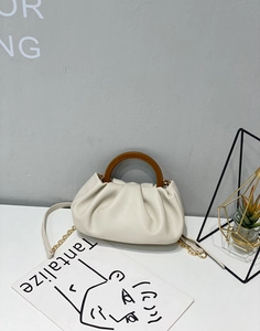 Close-up of cream pleated cloud bag with round wooden handle and gold chain strap