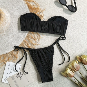 Close-up of pleated black bandeau bikini set with side-tie bottoms on a resort background