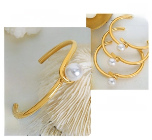 Macro detail of gold-plated geometric bangle with large white pearl on book background