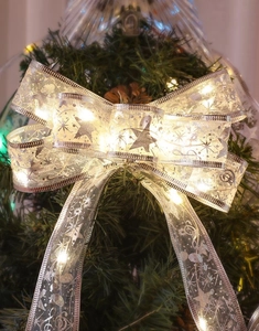 Close-up of silver Christmas bow with LED lights and star patterns on a festive tree