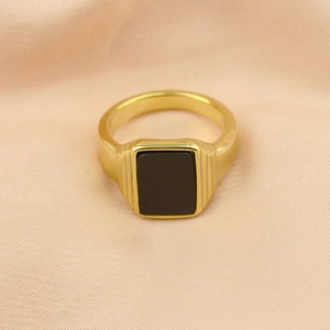Macro detail of gold-plated signet ring with black rectangular stone and striped texture