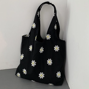 Detailed embroidery of white daisies with yellow centers on black canvas tote bag