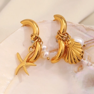 Detailed close-up of 18K gold-plated starfish and shell pendant earrings on a seashell