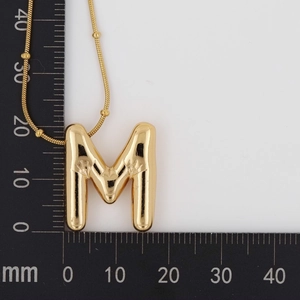 Size detail of gold 3D bubble letter M pendant with radial texture on a ruler