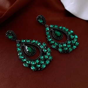 Macro view of vintage drop earrings with green rhinestones on dark velvet base