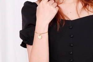 Detail of gold-plated stainless steel heart bracelet with Love engraving on female wrist