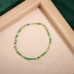 Detail of handmade colorful seed bead bracelet with green and gold accents on textured mat