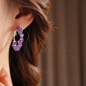 Detail of silver hoop earrings with purple zircon crystals worn by a model