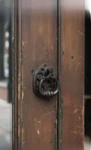 Detailed close-up of antique bronze door knocker on weathered wood with coffee bean plaque