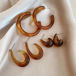 Detail view of amber resin earrings set on champagne satin fabric featuring three shapes