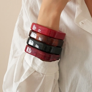 Close-up of resin geometric bangles in red, amber, and black on a white linen sleeve