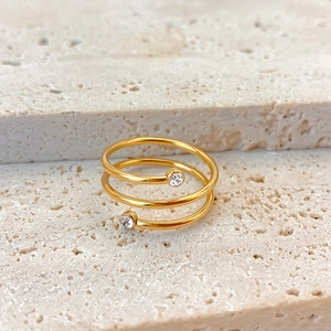 Detail eines goldenen Spiralrings mit Zirkonia-Akzenten auf natürlichem Steinuntergrund