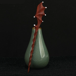 Detailed close-up of a carved sandalwood dragon wing hairpin in a celadon vase