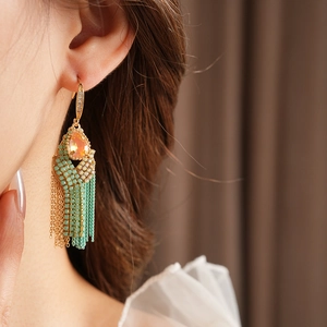 Detail of bohemian gold tassel earring with orange teardrop gemstone and turquoise beads