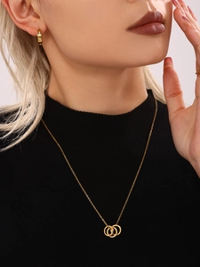 Close-up of model wearing gold triple-intertwined ring necklace and studded hoop earrings