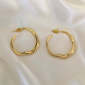 Irregular wavy gold hoop earrings displayed on elegant white silk background for women