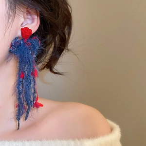 Dettaglio orecchini a rosa di velluto rosso con lunghe nappe blu su modella