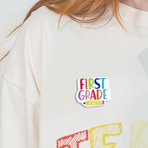 Colorful First Grade teacher brooch with yellow pencil design worn on a white sweater