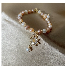 Detail of freshwater pearl bracelet featuring a zircon sunflower charm on silk background