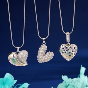 Three silver heart pendants with zircon inlay on snake chains against a blue floral background