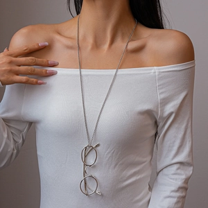 Detail of silver glasses pendant necklace worn on a white sweater as a long chain accessory