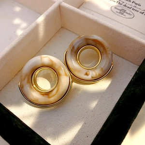Gros plan de boucles d'oreilles rétro texture ambre et bord doré sur velours beige
