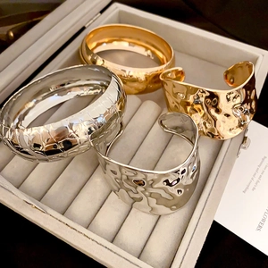 Macro view of gold and silver metallic bracelets with hammered and checkered textures in a tray