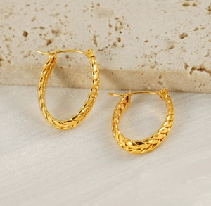 Close-up of golden oval hoop earrings featuring a vintage twisted woven metal texture