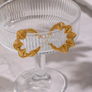 Detailed view of irregular pleated 18K gold earrings on a textured glass cup rim
