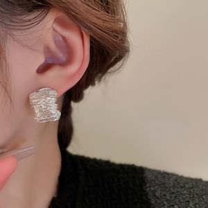 Close-up of geometric silver earrings with textured metallic pleats worn by a model
