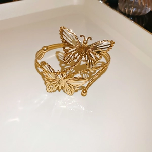 Detail of a hollow double butterfly gold metal cuff bracelet on a minimalist tray