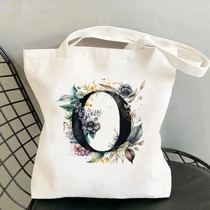 White canvas tote bag with floral letter O print on a black metal chair against grey wall