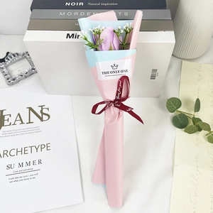 Detailed view of single purple soap rose in pink and blue wrap with red ribbon