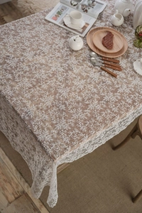 Detailed overhead shot of white lace tablecloth with floral embroidery on wooden table
