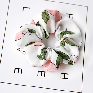 Detailed view of white fabric scrunchie with pink peach and green leaf pattern prints
