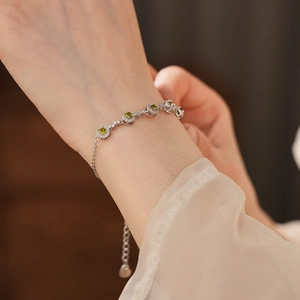Close-up of a silver-toned bracelet with green round zircon stones on a woman's wrist