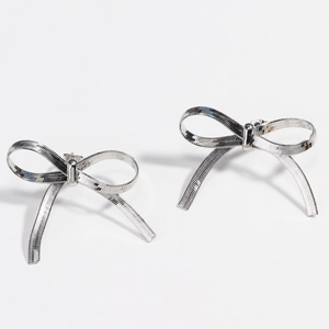 Detail of silver bow earrings featuring a textured metallic finish on white background