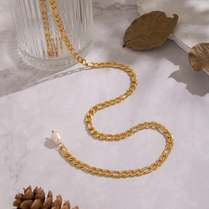Close-up of gold Figaro chain with a baroque natural pearl on marble surface