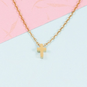 Close-up of minimalist golden stainless steel cross pendant necklace on a soft pastel background