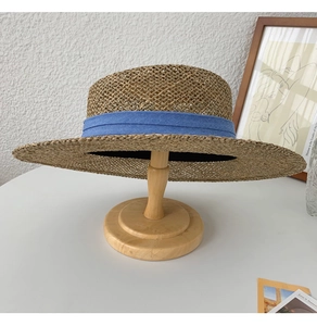 Detail of handmade straw hat with blue fabric ribbon and woven texture on wooden stand